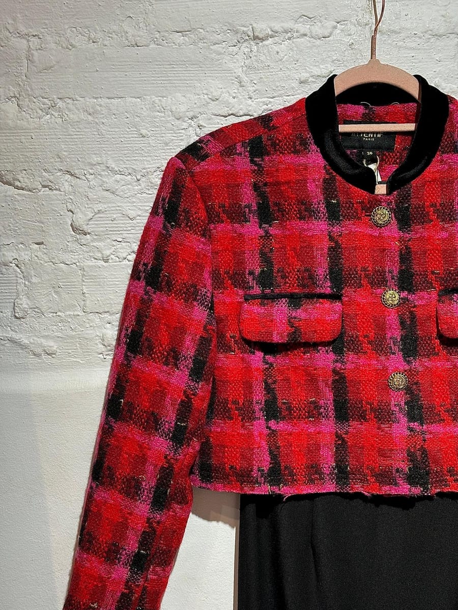 Chaqueta de tweed en rojo y fucsia colgada sobre pared de ladrillo blanco
