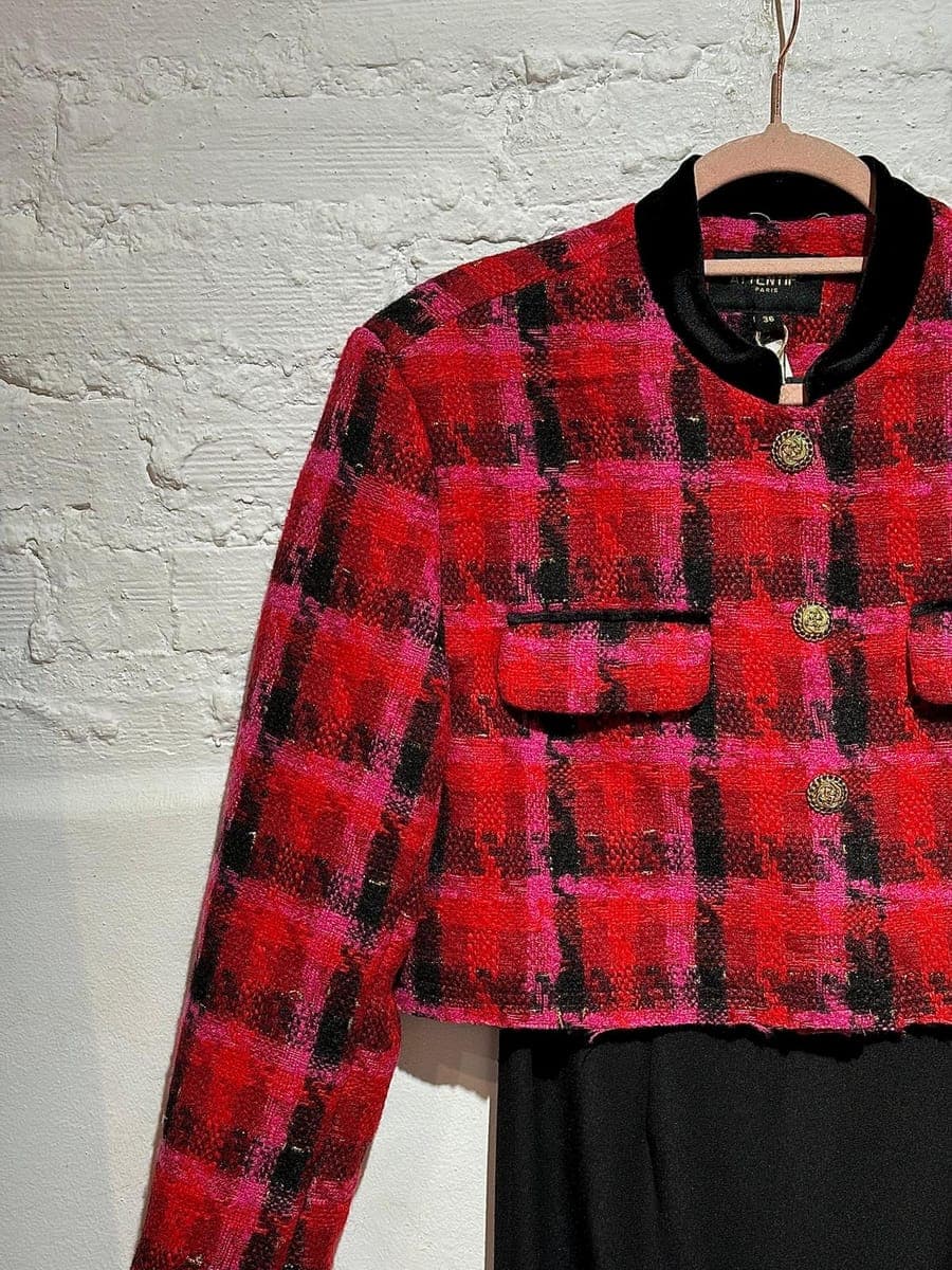 Chaqueta de tweed en rojo y fucsia colgada sobre pared de ladrillo blanco